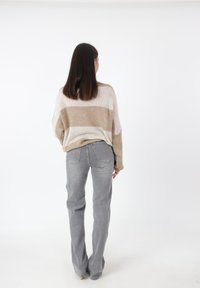 Overmaat, gestreepte trui in beige en room, gecombineerd met lichtgrijze flared jeans. Gladde textuur met zichtbare achterzakken.