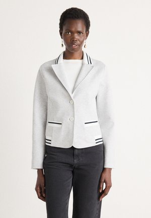 Grijze blazer van zachte stof met een gesneden kraag, twee knopen en gestreepte accenten op de kraag en zakken. Gecombineerd met zwarte broeken.