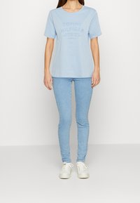 Vaaleansininen puuvillainen lyhythihainen T-paita, jossa kohokuvioitu 'TOMMY HILFIGER' -logo. Yhdistetty vaaleansinisiin skinny-farkkuihin ja valkoisiin tennareihin.