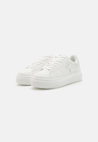 Hvite sneakers med en teksturert gummisåle, med en glatt syntetisk overdel, klassisk snøredesign og subtil branding på siden.