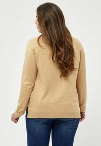 Maglione beige chiaro realizzato in materiale a maglia, con maniche lunghe e scollo rotondo. L'orlo è leggermente più lungo sul retro.