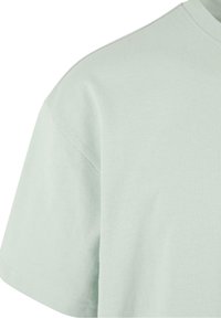 T-shirt vert clair à manches courtes, fabriqué en coton doux, avec un col rond et une texture lisse. Détail de couture visible aux épaules.