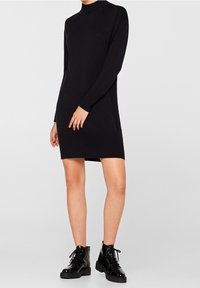 Robe tricotée noire à manches longues et col montant. Texture côtelée aux poignets et à l'ourlet, présente une coupe droite et une longueur mi-cuisse.