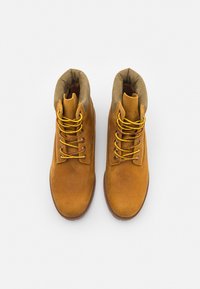 Botine din suede bej, cu un finisaj neted, vârf rotund și guler căptușit. Au șireturi galbene și maro, cu ochiuri metalice.