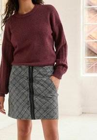 Bordowy sweter dzianinowy z prążkowanymi rękawami zestawiony z ołówkową spódnicą w kratę, wyposażoną w zamek błyskawiczny z przodu oraz dwie boczne kieszenie.