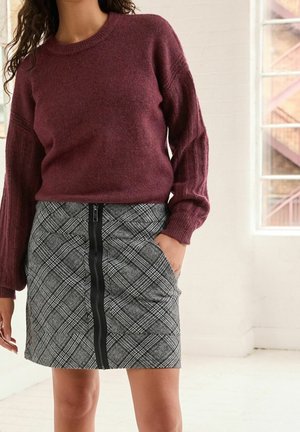 Burgundský pletený svetr s ribovanými rukávy v kombinaci s kostkovanou tužkovou sukní s předním zipem a dvěma bočními kapsami.