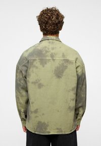 Olivengroen gebrushd katoen overshirt met een tie-dye effect, knoopmanchetten en een relaxte pasvorm. Gedetailleerde stiksels langs de schouders.