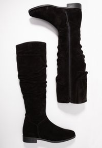 Czarne zamszowe wysokie botki z luźnym krojem, bocznym zamkiem błyskawicznym i płaską podeszwą. Górna część jest gładka i miękka w dotyku.