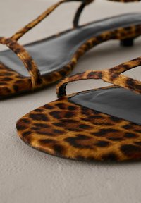 Flat sandaler med leopardmönster som har en övre del i konstläder, svart läderinlägg och en elegant cross-strap-design med låg klack.
