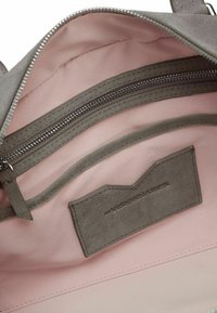 Interno di una borsa in camoscio grigio con foderina rosa, dotato di un compartimento con zip e di un'etichetta in tessuto con testo in rilievo.