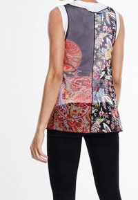 Žena v bezrukávovém topu s různobarevnými květinovými a paisley vzory, v kombinaci s černými přiléhavými kalhotami, ukazující se zezadu.