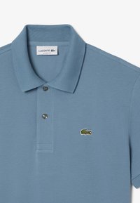 Koszulka polo w jasnoniebieskim kolorze z bawełny o klasycznym kroju, z prążkowanym kołnierzykiem, trzema guzikami oraz zielonym logo krokodyla na piersi.