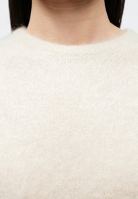 Pulover tricotat bej deschis, cu decolteu rotund, având o textură moale și pufoasă și un model subtil, fin pe toată suprafața.