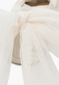Close-up of a white sneaker featuring a soft, sheer bow made of lightweight fabric, emphasizing its delicate design and texture.