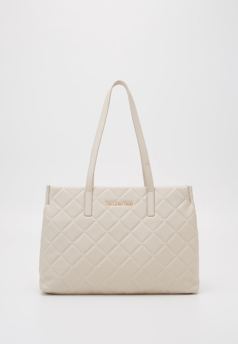 Sac cabas en cuir matelassé beige avec deux poignées et ferrures dorées. Présente un logo embossé sur le devant et une forme rectangulaire.