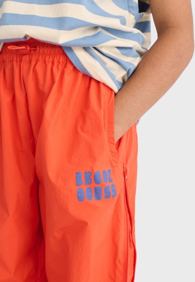 Enfant portant un short orange vif avec un cordon de serrage à la taille et une fermeture éclair de poche, associé à une chemise rayée bleue et blanche.