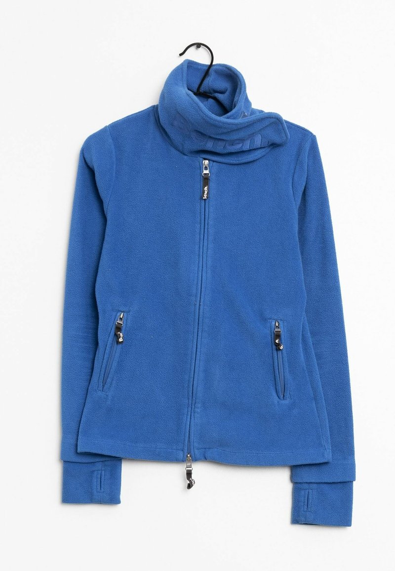 Veste en polaire bleue avec col montant, fermeture éclair intégrale à l'avant, poches latérales zippées et ouvertures pour les pouces sur les longues manches, suspendue sur un cintre noir.
