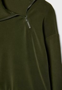 Tamno maslinasto zelena dukserica s polu-zip ovratnikom, mekane teksture i opuštenog kroja. Ima glatku površinu i minimalne detalje šivanja.