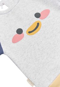 Camisa de bebé gris claro con un diseño abstracto de cara sonriente en negro, rosa y amarillo, y un puño amarillo en la manga.