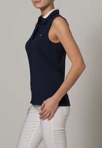 Laivastonsininen, hihaton poolopaita, jossa valkoinen kaulus, tehty pehmeästä kankaasta. Slim fit -leikkaus ja hillitty rintalogo.