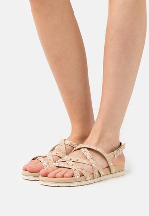 Sandales beige à lanières avec des accents tressés, des sangles texturées, des clous décoratifs et une semelle plate et coussinée. Fermeture par boucle à la cheville.