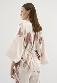 Beige szatén kimono felső rózsaszín absztrakt mintákkal, széles ujjakkal és állítható derekú zsinórral.