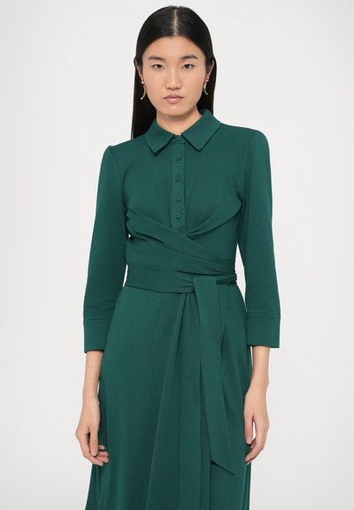 Πράσινο φόρεμα με γιακά, μακριά μανίκια και δεμένη μέση. Κατασκευασμένο από λείο ύφασμα με λεπτομέρειες κουμπιών στο εμπρόσθιο μέρος.