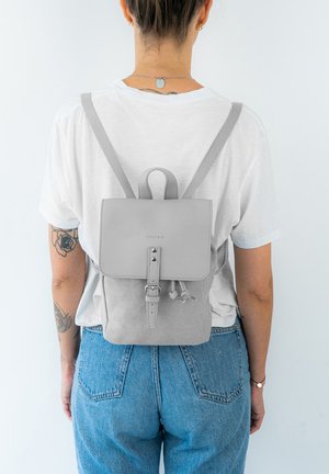 Kleiner grauer Rucksack aus Wildleder und Leder, mit Klappenverschluss, verstellbaren Riemen und minimalistischem Design mit Schnallenakzenten.