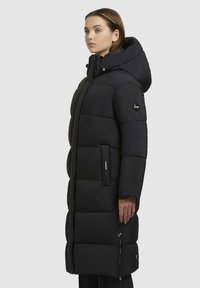 Sort pufferjakke med hætte, med en quiltet design, sidelommer og en lynlåsdetalje. Glat tekstur og knælang model.
