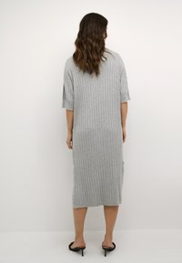 Graues, geripptes Strickkleid mit kurzen Ärmeln und seitlichen Schlitzen, das bis zur Mitte der Waden reicht. Kombiniert mit schwarzen, mit Absatz versehenen Sandalen. Minimalistisches Design.
