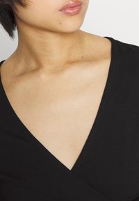 Svart omslagstopp med djup V-ringning och korta ärmar, tillverkad i ett mjukt, stretchigt tyg som framhäver en subtil lyster.