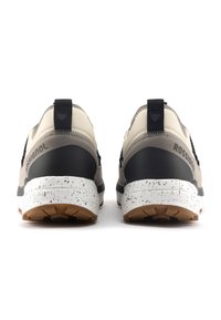 Beige und schwarze Sportschuhe verfügen über ein strukturiertes Obermaterial, eine kontrastierende Gummisohle mit gesprenkeltem Detail und ein auffälliges Markenlogo an der Ferse.