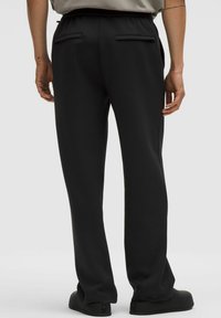Zwarte broek met een relaxte pasvorm, elastische tailleband en achterzakken, weergegeven vanuit de achterkant, waarbij de stoftextuur en de afwerking worden benadrukt.