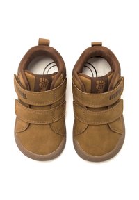 Scarpe per bambini in suede marrone con doppie cinghie in Velcro, punta arrotondata e collo imbottito. Suola piatta in gomma con una presa testurizzata, branding minimo.