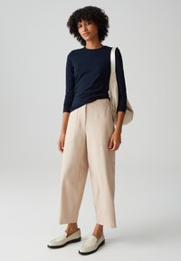 Maglietta a maniche lunghe blu abbinata a pantaloni larghi color beige chiaro. Mocassini chiari completano il look. Design semplice e tessuto morbido.