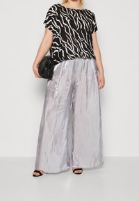Top a strisce zebra in bianco e nero con maniche corte, abbinato a pantaloni larghi in argento lucido. Borsa nera in tessuto testurizzato e sandali neri.