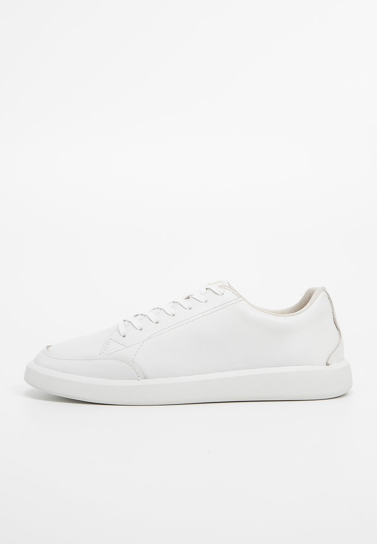 Sneaker en cuir blanc avec une finition lisse, bout rond, couture discrète et design à lacets. Présente un intérieur beige doux et une semelle en caoutchouc plate.
