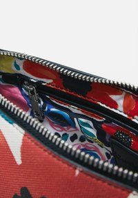 Interno di una borsa con motivo floreale multicolore, dotata di una cerniera nera e di un design esterno contrastante in rosso e bianco. Tessuto testurizzato.