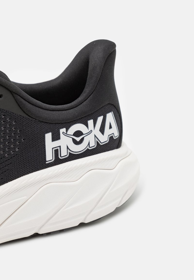 Czarny but sportowy z przewiewną siateczką, wyraźnym białym logo, amortyzowaną podeszwą i teksturowanymi akcentami na pięcie.