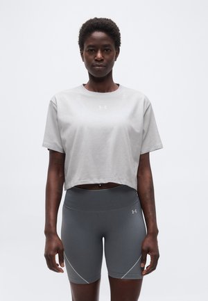 Femme portant un t-shirt court gris clair et un short de sport ajusté gris foncé, debout devant un fond blanc uni.