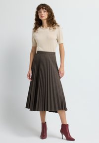 Beige lyhythihainen neule, jossa on teksturoitu kaula-aukko, yhdistetty tummanruskeaan laskostettuun midihameeseen ja viininpunaisiin nilkkavBootseihin.