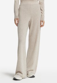 Beige vida byxor i mjukt tyg med en slät textur, med hög midja och sidofickor. Matcher med ljusa sneakers.