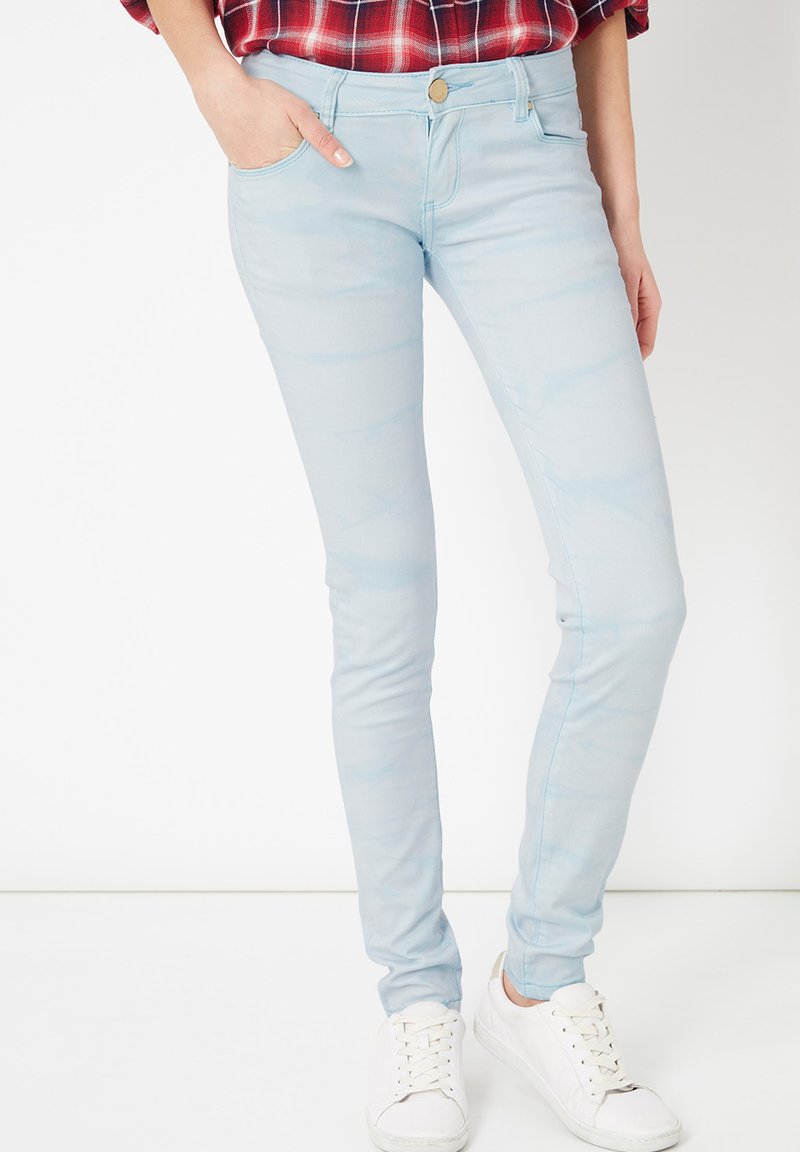 Jeans ajustados de color azul claro hechos de denim, con un sutil patrón desvaído, cinco bolsillos y una cintura con botón, combinados con zapatillas blancas.