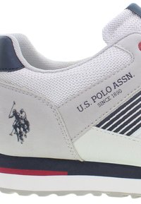 Adidaș gri cu țesătură texturată, accente din piele și o talpă albă. Are un logo și un design în dungi pe lateral. Detalii roșii pe călcâi.