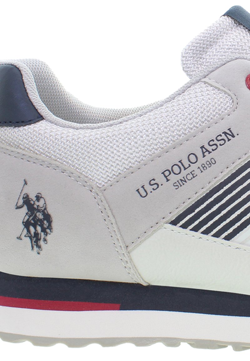 Baskets grises avec un tissu texturé, des accents en cuir et une semelle blanche. Présente un logo et un design rayé sur le côté. Détails rouges sur le talon.