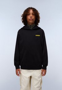 Felpa nera con cappuccio e tasca frontale, con orlo curvo e un logo giallo sul lato sinistro del petto. Abbinata a pantaloni cargo color crema.