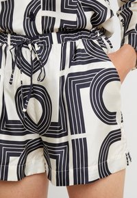 Unisex shorts i ett krämfärgat tyg med ett djärvt geometriskt mönster i marinblått. Elastisk midja med dragsko och sidofickor. Slät textur.