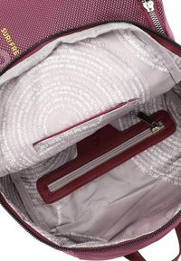 Sac à dos en tissu bordeaux avec une ouverture zippée. L'intérieur présente un revêtement gris clair avec du texte imprimé et une petite poche zippée.