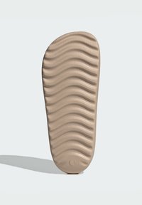 Beige gummiskoinlägg med vågig textur, rund tå och en cirkulär indentering vid hälen.