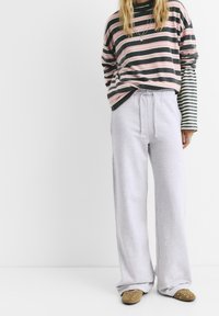 Pasiasty longsleeve w kolorze ciemnoszarym, różowym i białym; jasnoszare dresy; brązowe półbuty na stopę z okrągłymi akcentami; luźny krój.